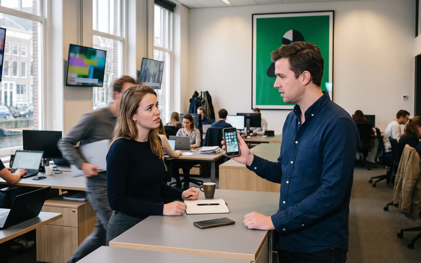 Een open redactievloer: de directeur driekwart van achteren, een oude telefoon uit 2016 in zijn hand, grote schermen met de huidige campagne erachter.